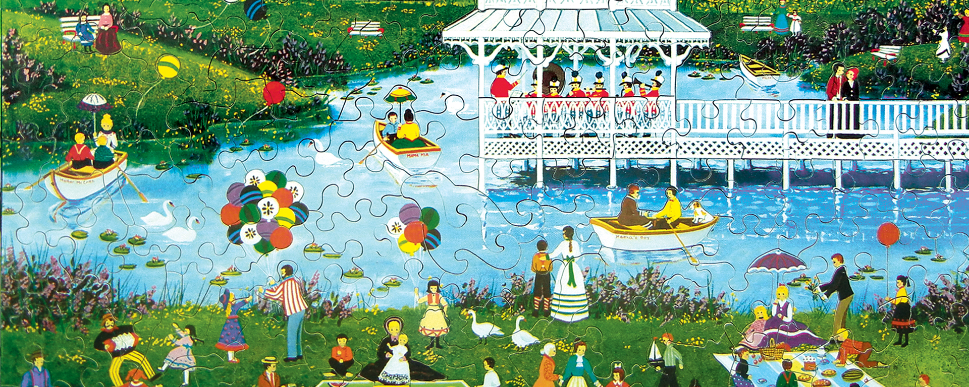 Wooden jigsaw Mother’s Day puzzle depicting a day at the park. The park is full of people doing activities in and around the pond in the center.